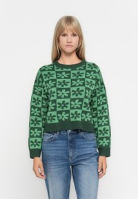 Green knitted sweater with a cropped design, featuring a floral pattern in darker green. Ribbed neckline and cuffs add texture.