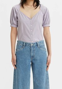 Lila och vit rutmönstrad kortärmad blus med v-ringning och knäppning fram, kombinerad med höga, vida ljusblå jeans.