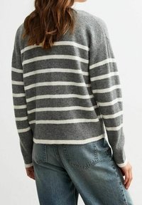 Kobieta z długimi brązowymi włosami, ubrana w szaro-białą w paski bluzę i niebieskie dżinsy, pokazana plecami na białym tle.