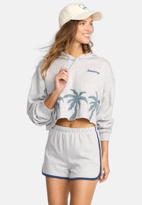Grijze cropped hoodie met palmboomprint, gecombineerd met grijze shorts met een blauwe rand. Wordt geleverd met een crèmekleurige baseballcap.