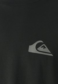 Crna pamučna majica s mat sivim logotipom na lijevoj strani grudi, s rebrastim izrezom i glatkom teksturom.