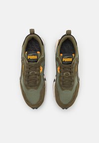 Zapatillas deportivas verdes y beige con tela texturizada y superposición de ante. Presentan detalles en negro y un logo naranja en la lengüeta.