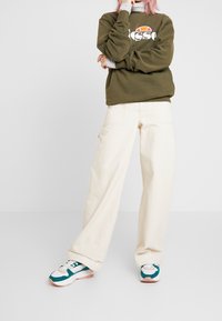 Green sweatshirt with white logo, cream wide-leg pants, and multicolored sneakers featuring teal and pink accents. Casual athletic wear.