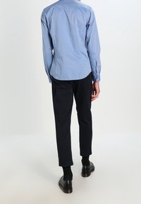 Světle modrá pruhovaná košile s dlouhým rukávem, černé kalhoty rovného střihu a černé boty. Košile má límec a kalhoty mají volný střih.