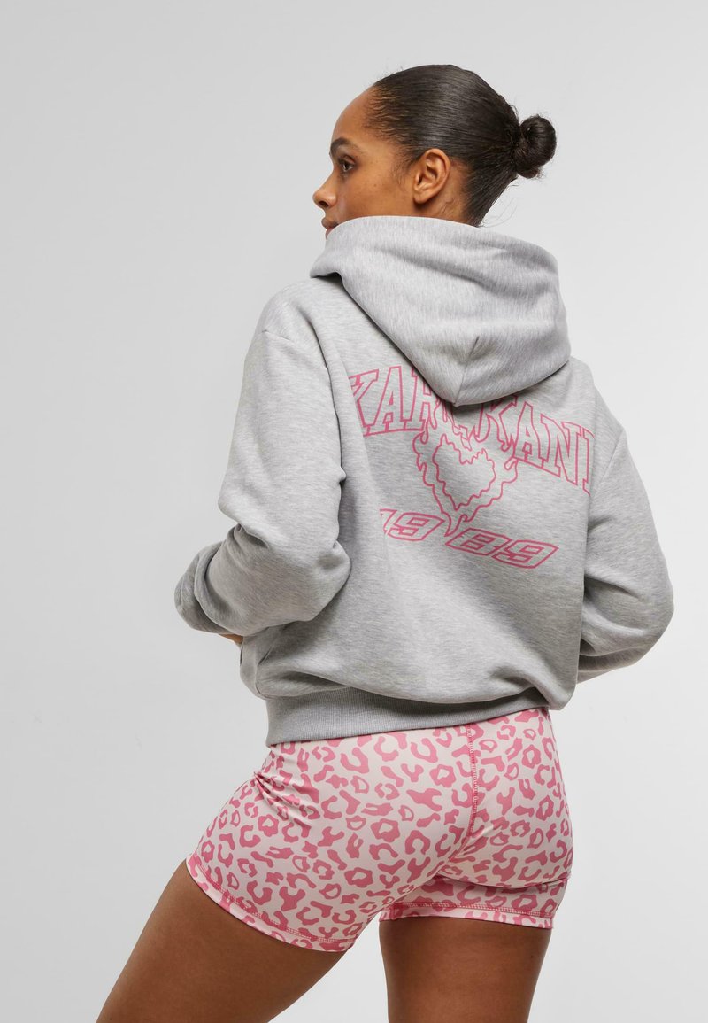 Grå hettegenser med rosa grafisk design og tekst på baksiden, sammen med rosa leopardmønstrede shorts. Mykt stoff, avslappet passform.