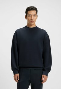 Navy blue sweatshirt, oversized fit, round neckline, soft fabric, ribbed cuffs, smooth texture, paired with matching trousers.