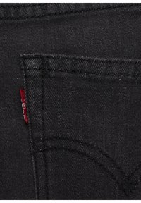 Tela de mezclilla negra con un bolsillo trasero visible, que presenta una pequeña etiqueta roja y costuras en contraste a lo largo de los bordes y el contorno del bolsillo.