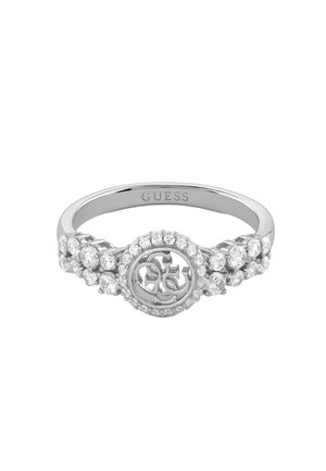 Srebrn prsten Guess s okruglim logom u sredini okružen malim prozirnim kamenjem, dodatni kamenčići duž stranica prstena.