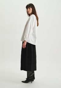 Chemise blanche à manches longues associée à une jupe midi noire à volants et des bottes noires montantes, avec une coupe ample et des poignets froncés.