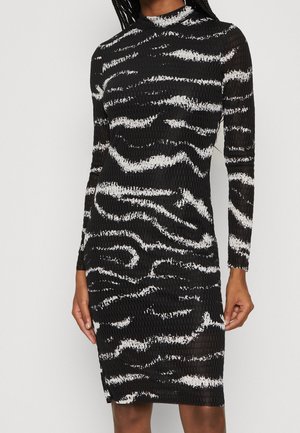 Robe moulante texturée noire et blanche à manches longues avec un motif abstrait d'imprimé animal, portée par une personne sur un fond clair uni.