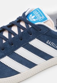 Marine suede sportschoen met witte leren strepen. Geribbelde buitenzool en een blauwe label op de tong. Merknnaam "Gazelle" in witte letters.