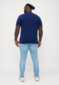 Camiseta de algodón azul marino con mangas cortas y cuello redondo; combinada con jeans de color azul claro. Textura suave, corte estándar, diseño minimalista.