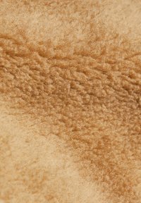 Gros plan sur un tissu polaire brun clair, doux et texturé, avec des fibres denses et bouclées et une surface légèrement irrégulière.