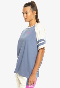 Modrá a smotanová raglánová tričká s ružovým logom, so prúžkovanými rukávmi, voľným strihom a mäkkým bavlneným materiálom.