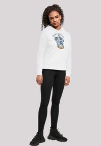 Felpa bianca con un design blu e oro del crest di Ravenclaw, abbinata a leggings neri e scarpe da ginnastica nere.