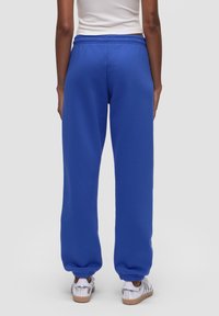 Niebieskie dresy wykonane z miękkiego materiału, z elastycznym pasem i ściąganymi mankietami, połączone z srebrnym obuwiem i białą górą.