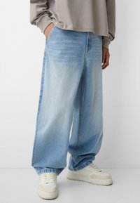 Himmelblaue weit geschnittene Jeans aus Denim, mit einer leicht verblassten Textur und elastischen Bündchen, kombiniert mit weißen Sneakers.