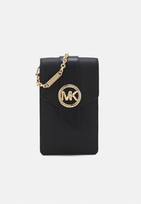 Černá kožená crossbody taška na telefon se zlatým řetězovým popruhem a výrazným kruhovým logem na přední straně, s klopovým uzávěrem.