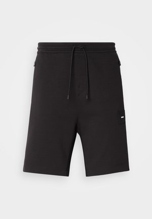 Pantaloni corti neri realizzati in tessuto morbido, dotati di una vita elastica con cordino, tasche laterali e una piccola etichetta con logo sul lato sinistro.