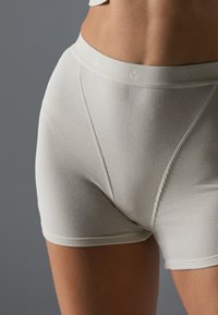 Pantaloni scurți bej cu nervuri, având o talie moale, ce prezintă un branding subtil. Materialul pare neted, cu o ajustare confortabilă și fără cusături vizibile.