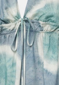 Tissu tie-dye bleu et blanc avec des sections élastiques froncées et un nœud lié au centre, montrant texture et variation de couleur.