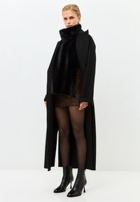 Manteau long noir, col en fausse fourrure, jupe à imprimé léopard, collants transparents, bottines noires à talons hauts, texture lisse, design moderne.
