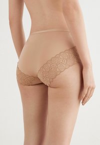 Nude spetsunderkläder med intrikata blommönster, en vågig kant och mjuk tyg, designade för en bekväm passform.
