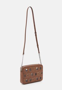 Brun læder crossbody taske med udskæring i logo mønster, sølv hardware, justerbar rem og kontrasterende syninger.