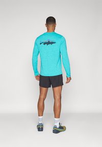 Light blue long-sleeve shirt with a black fish graphic on the back, paired with black shorts and greenish shoes. Smooth fabric texture.