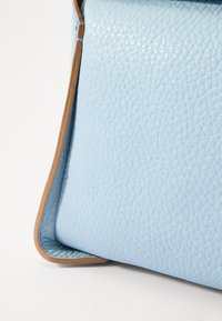 Borsa a mano in pelle azzurro chiaro con superficie texture, dettagli a contrasto in tan e una forma strutturata. La superficie ha una finitura a ciottolo.