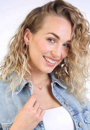 Zilveren V-vormige ketting en stud oorbellen, gedragen met een spijkerjack. Model heeft golvend, blond haar en een natuurlijke make-uplook.