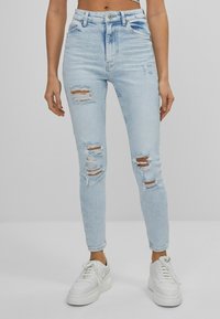 Ljusblå högmidjade jeans med slitna detaljer vid knäna. Kombineras med vita klumpiga sneakers. Har en klassisk femfickdesign.