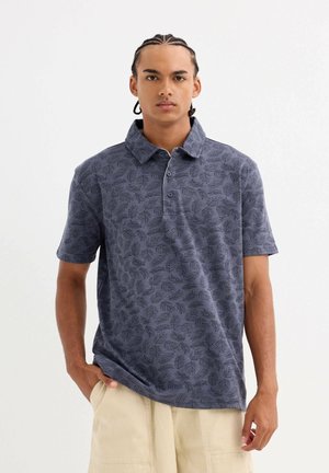 Polo de manga corta en color marino con un patrón de hojas, confeccionado en una tela texturizada, con cuello y tapeta de tres botones.