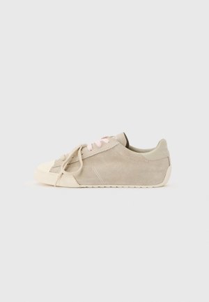 Beige suède lage sneaker met lichtroze veters, een off-white rubberen zool en een afgeronde neus tegen een effen lichte achtergrond.