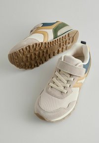 Beige og grønne sportsko med teksturerede overflader, stof- og ruskindsmaterialer. Har en velcro-rem og gummi ydersål.