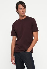 Bordeaux katoenen t-shirt met ronde hals en korte mouwen, gecombineerd met donkere spijkerbroeken. Minimale stijl, geen zichtbare patronen of graphics.