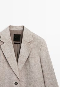 Béžové sako s texturou, klopovým límcem se zářezem, zapínáním na jeden knoflík, náprsní kapsou a štítkem "Massimo Dutti" uvnitř límce.