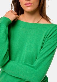 Grüner Strickpullover mit einem lockeren, schulterfreien Design und langen Ärmeln. Weiche Textur, mit einer entspannten Passform und einem subtilen Glanz.