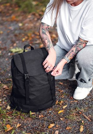 Black fabric backpack with top flap, adjustable straps, front pocket, and buckle closure. Textured material with minimalist design.