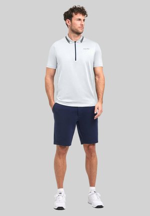 Le polo pour homme gris clair présente un col zippé, des accents noirs et un logo. Assorti avec un short bleu marine et des baskets blanches.