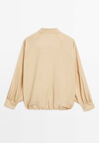 Beige lätt blus med krage, raglanärmar, elastiskt midjeband och knäppte manschetter. Slät textur, avslappnad passform och minimalistisk design.