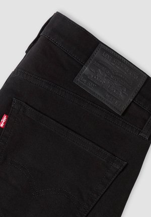 Schwarze Levi's Jeans gefaltet, mit sichtbarer Gesäßtasche mit rotem Levi's-Label und schwarzem Leder-Levi's Markenpatch über der Tasche.