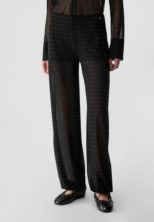 Black sheer wide-leg pants with small white dots, worn with matching sheer shirt and black ballet flats.
