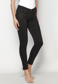 Black skinny jeans with embroidered leaf patterns on the front pockets and silver hardware. The fabric has a smooth, stretchy texture.