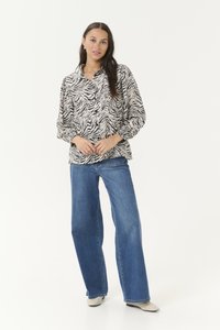 Button-down shirt with a black and white zebra print, paired with wide-leg blue jeans. Model wears cream-colored shoes. Plain white background.