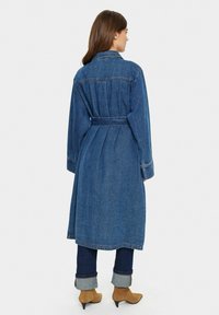 Dlhý denimový kabát s opaskom v páse, golierom a dlhými rukávmi, v hlbokej modrej farbe a s jemnými švou.
