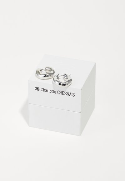 Pair of polished silver hoop earrings with a modern, curved square shape, resting on a white Charlotte Chesnais branded box.
