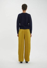 Pull en maille bleu marine à col rond, associé à un pantalon large moutarde. Texture lisse avec un ourlet côtelé et une couleur unie.