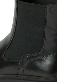 Bottine en cuir noir à cheville avec panneaux élastiques sur les côtés. Texture lisse avec des accents cousus et une semelle en caoutchouc. Aucun motif ou matériel visible.