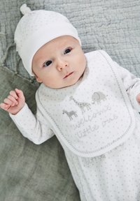 Biely overal s šedými bodkami, obsahujúci šedé zvieracie motívy a text "vitaj, malé". K tomu ladiaca biela čiapka.